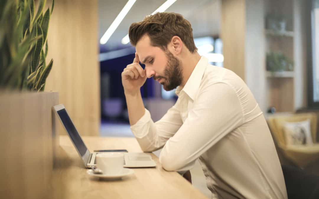 man with hand on temple looking at laptop