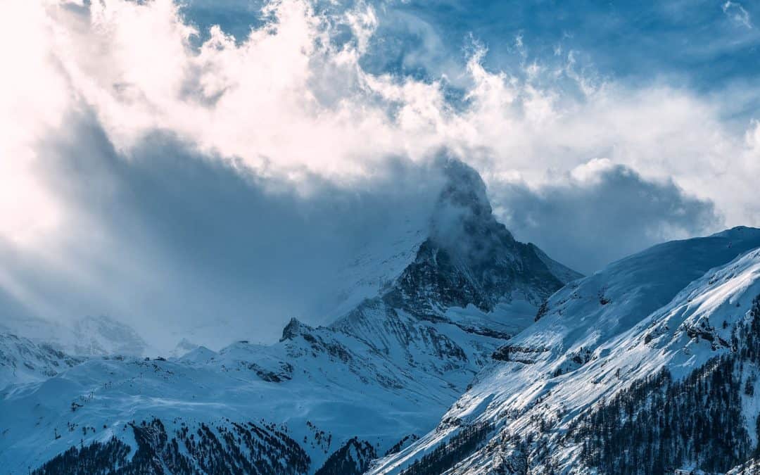 snowy mountain peaks under cloudy sky in sunlight